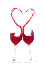 Two glasses of red wine in toasting gesture with heart splashing. Heart splash from two glasses of red wine isolated on white
