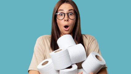 Cute woman holds bunch of rolls with toilet paper, she opened her mouth in a surprise