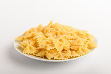 Dried Farfalle Rigate Italian pasta on a plate ready to be cooked, isolated on a white table, top view or flat lay of healthy food 
