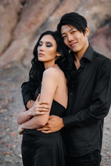 An Asian couple in love in black leather clothes walk in nature among the trees. Style, fashion, love