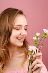 Obraz na płótnie Canvas Close-up beauty portrait of an attractive young woman in a summer dress holding a carnation flower in her hand. A girl with light wavy hair. Isolated on a pink background