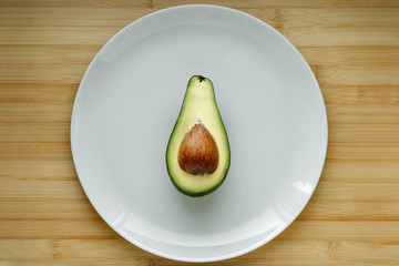 A half of fresh green avocado isolated in the middle on the plate on wooden table  top view. Closeup.