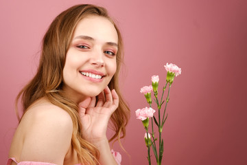 Close-up beauty portrait of an attractive young woman in a summer dress holding a carnation flower in her hand. A girl with light wavy hair. Isolated on a pink background