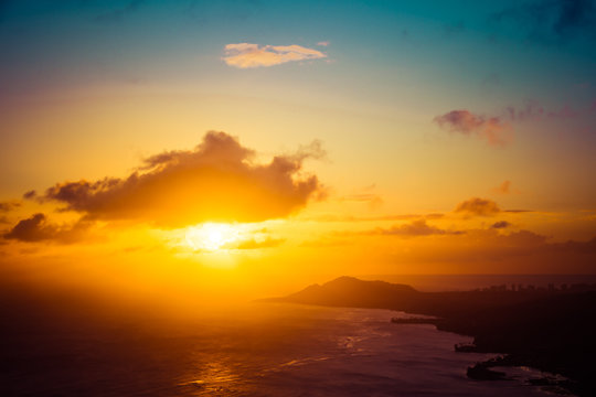 A sunset over the Hawaiian Island of Oahu as seen from a mountain top with the city of Waikiki Beach and Diamond Head in the distance.  Image captured from the summit of Koko Head Crater.