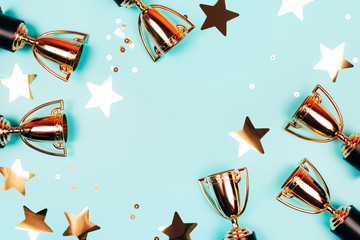 Golden cups of winner with shiny confetti on a blue background with copy space. Flat lay style. - 336131328