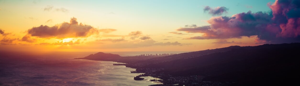 A panorama of a sunset over the Hawaiian Island of Oahu as seen from a mountain top with the city of Waikiki Beach and Diamond Head in the distance.  Image captured from the summit of Koko Head Crater