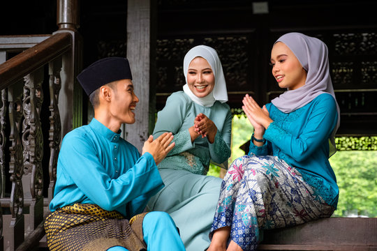 A group of malay muslim people in traditional costume showing greeting gesture during Aidilfitri celebration at terrace of traditional wooden house