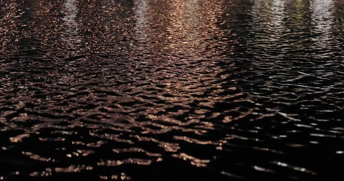 Pond water surface at night with steet lamps reflecting on ripples