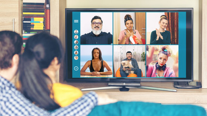 Millennial couple having fun on video call from home with multiracial happy friends from all over...
