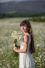 Naklejka na ściany i meble Beautiful teen girl on a walk in a daisy field in a white dress