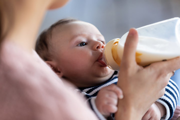 Mother feeding her baby son with feeding bottle while sitting on sofa at home.