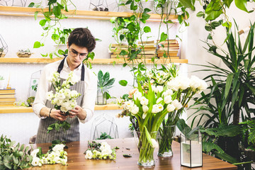 Attractive young male florist with glasses and apron works in a flower shop. pruning flower stems and preparing for bouquet assembly