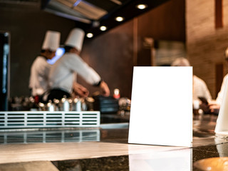mockup of a food menu list stand on wooden table inside restaurant with chef cooking fresh food...