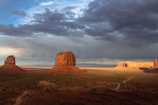 A storm leaving the scenic view of The Mittens and Merrick Butte from John Wayne's Point during the golden hour at sunset in the Oljato Navajo Monument Valley, Arizona USA