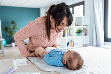 Smiling young mother has fun with little baby while changing his nappy at home.