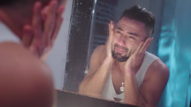 the guy looks sadly in the mirror.guy cries looking at the mirror
