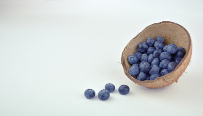 Fresh blueberries in a coconut shell as a cup on white background. Space for text