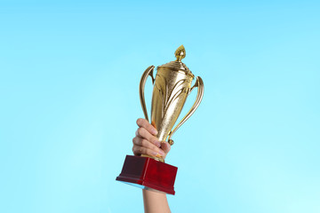 Woman holding gold trophy cup on light blue background, closeup
