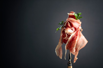 Thin sliced prosciutto with parsley on a fork. Traditional Italian cuisine. - obrazy, fototapety, plakaty