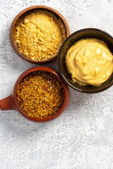Fototapeta na wymiar Different mustard: mustard powder, Dijon mustard and hot mustard in bowls on a gray concrete background top view.