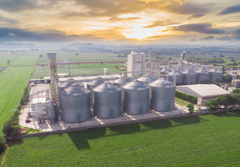 Aerial view of drone,Agricultural Silos - Building Exterior, Storage and drying of grains, wheat, corn, soy, sunflower against the golden sky with rice fields.