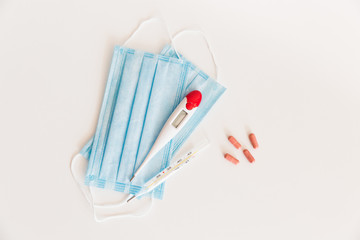 Medical protective mask with a thermometer on white background with pills. A disposable surgical face mask. Healthcare and medical concept.
Prevention of the Covid-19 pandemic virus. Quarantine.