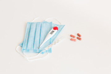 Medical protective mask with a thermometer on white background with pills. A disposable surgical face mask. Healthcare and medical concept.
Prevention of the Covid-19 pandemic virus. Quarantine.