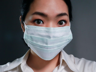 Close up portrait of Asian woman wearing a surgical face mask  looking at the camera with a calm serious expression. 