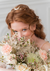 A wedding flower bouquet made of white roses and other flowers is held in her hands by a shapely redhead bride girl in defocus.