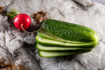 scharfe rote Radieschen und Gartengurke liegen auf weißem Stein