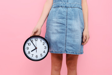 hands holding a wall clock on an isolated pink background