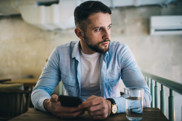 Contemplative hipster guy in casual wear concentrated on problem solution sitting with coffee cup on break, pensive caucasian 20s man writer thinking about creative ideas in cafeteria interior