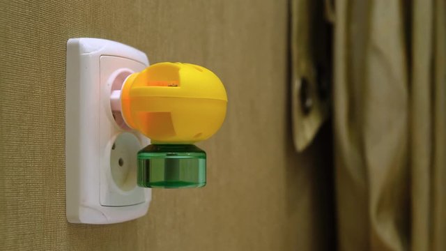 Close-Up of Electric Liquid Anti-Insects Fumigator Into Electic Outlet on a Wall in a room. Camera moving, dolly shoot.