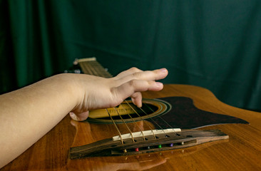 The boy tries to tune and play an acoustic guitar, playing the strings with his fingers.