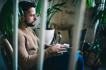 Serious pensive handsome guy sitting in cafe interior with technology for freelance job, thoughtful male blogger concentrated on creating publication and content working remotely in coffee shop