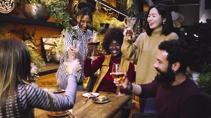  A group of friends from various ethnic groups enjoy happily and toast in a restaurant and bar with a very careful and elegant decoration

