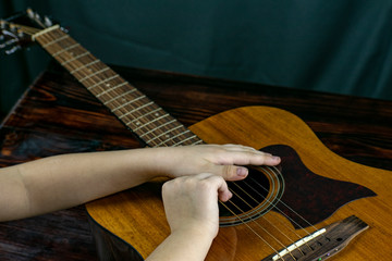 The boy tries to tune and play an acoustic guitar, playing the strings with his fingers.