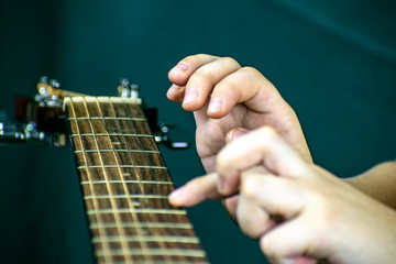 The boy tries to tune and play an acoustic guitar, playing the strings with his fingers.