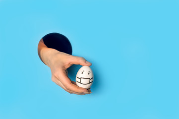 Woman's hand holds egg through hole in blue paper