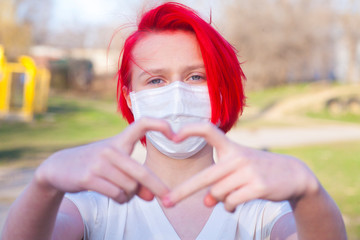 Red hair teenage girl wearing a medical mask shows the heart symbol love to fight and strong encourage health care from Covid 19