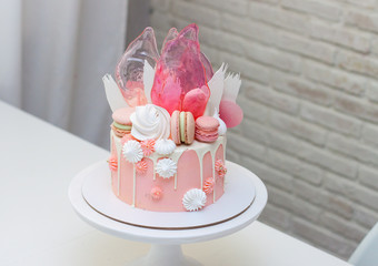 Modern pink cake with chocolate decor, caramel, french macaroons, meringues and waffle paper. White background