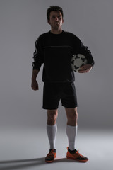 Fototapeta premium Soccer player in a black sportswear holding soccer ball in hands looking at the camera