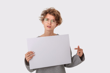 Concerned young woman with eyeglass holding empty blank paper board with copy space