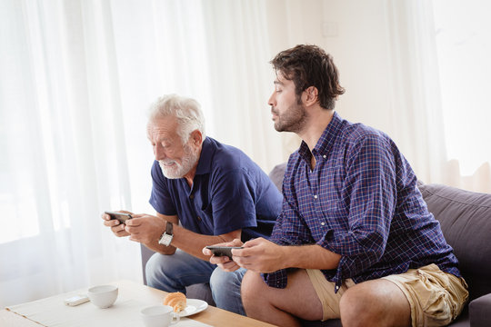 Grandfather elder happy enjoy moment fun with his son at home playing mobile game together.