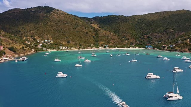 Drone aerial tracking shot over scenic tropical harbor with sailboats (Jost Van Dyke, British Virgin Islands)