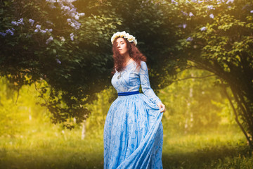 Attractive woman in a blue magnificent dress walks in the park against the background of blooming...