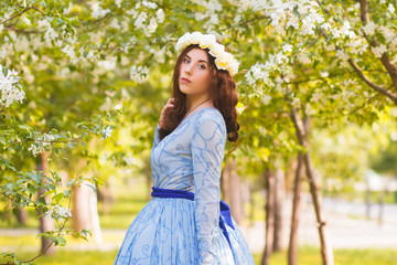 A beautiful woman in a blue puffy dress with a rim of white flowers on her head walks through the...