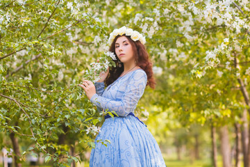 A beautiful woman in a blue puffy dress with a rim of white flowers on her head walks through the...
