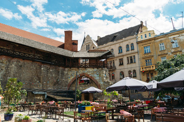 Sunny scenery of yard with stone wall and empty cafe in Ukrainian town.Coffee house at noon in Lviv.  Old city street with nobody. Restaurant with tables under open sky. Summer in capital of Ukraine.