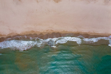 Aerial drone top-down photo and view of sea waves hitting rocks on the beach with turquoise sea water. Amazing rock cliff seascape in the Spanich coastline.